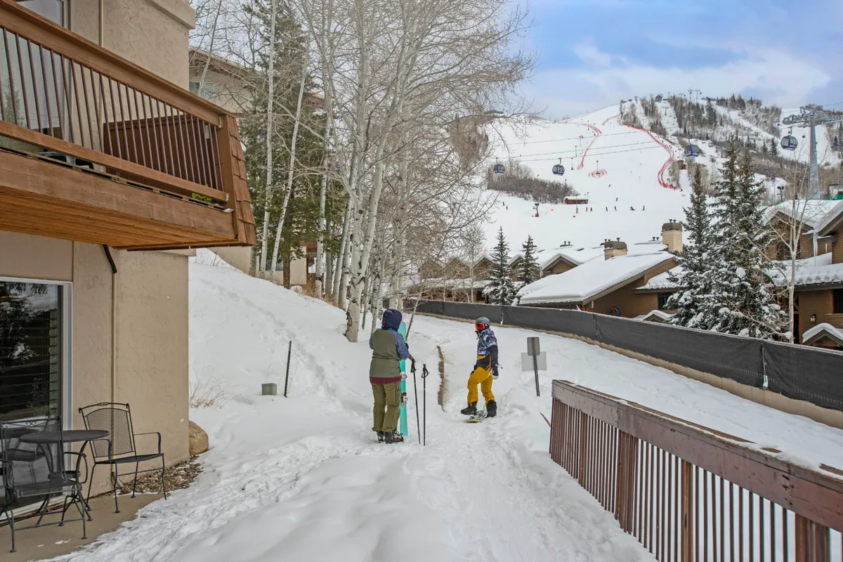 An exterior winter scene with skiers preparing for the slopes against a backdrop of snow-covered landscape and ski lifts. The energy is lively, with people gearing up for adventure just outside the property.