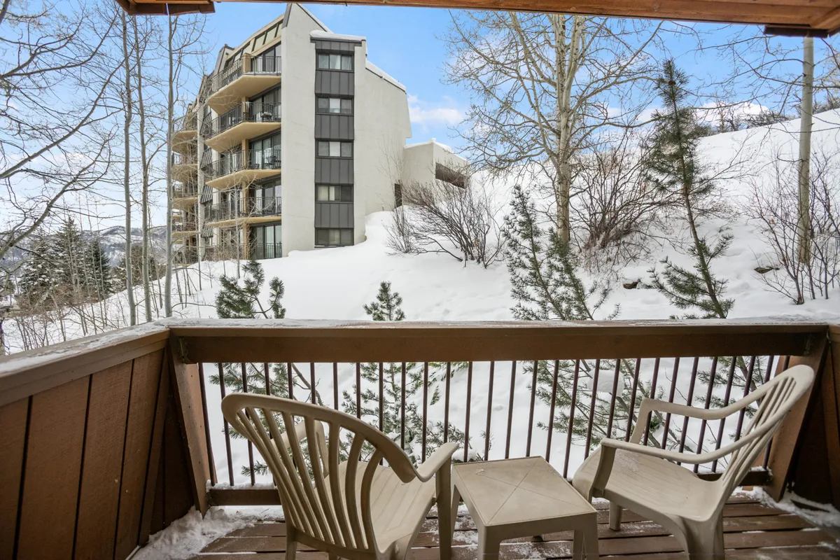 A private balcony overlooking a snowy expanse framed by trees and neighboring buildings. The serene setting showcases a perfect vantage point for wildlife spotting or simply relaxing after a day of outdoor activity.