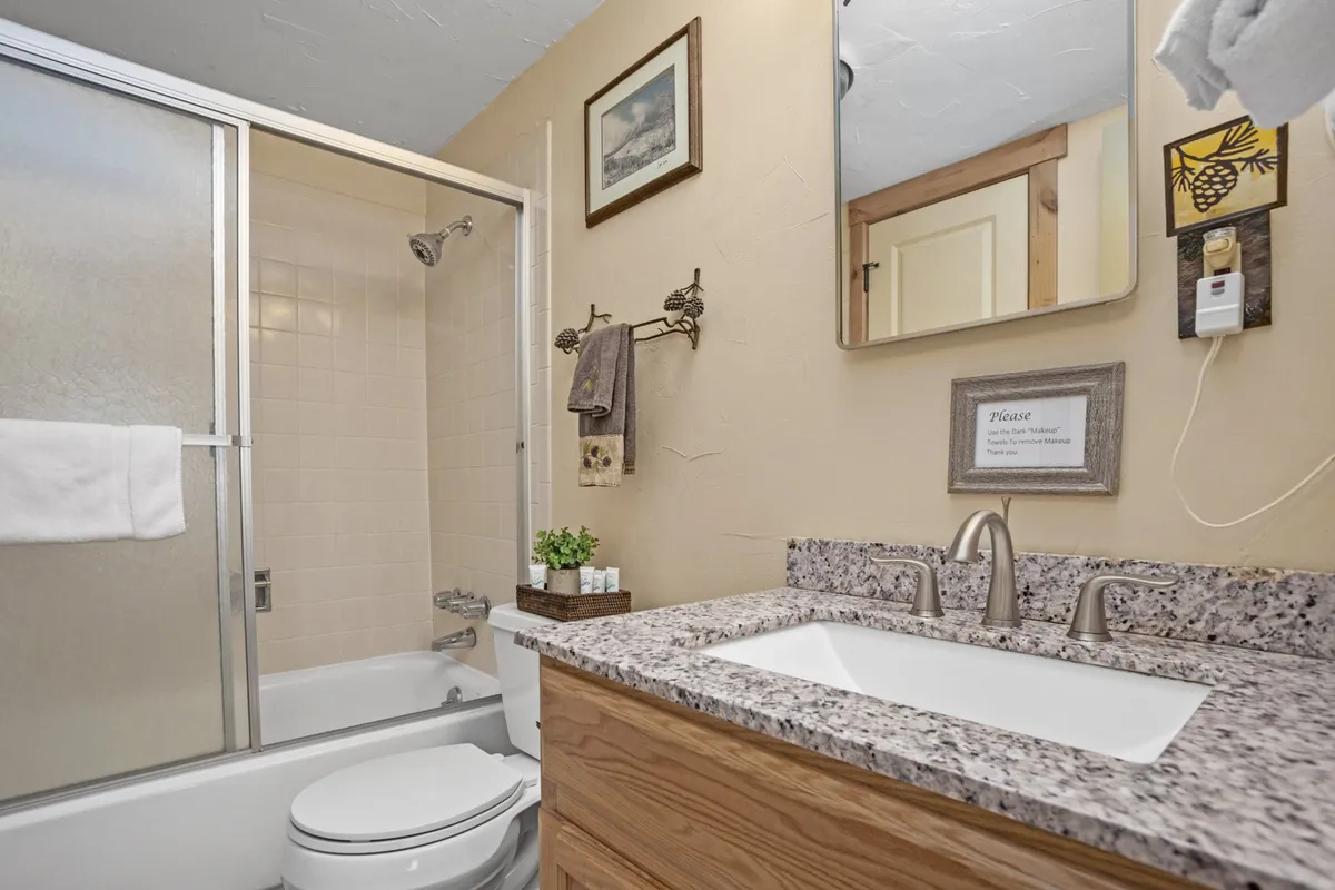 A spa-like bathroom is shown, complete with a sleek granite countertop, a large mirror, a glass shower enclosure, tasteful framed artwork, and a towel rack. The light and decor evoke calm and serenity.