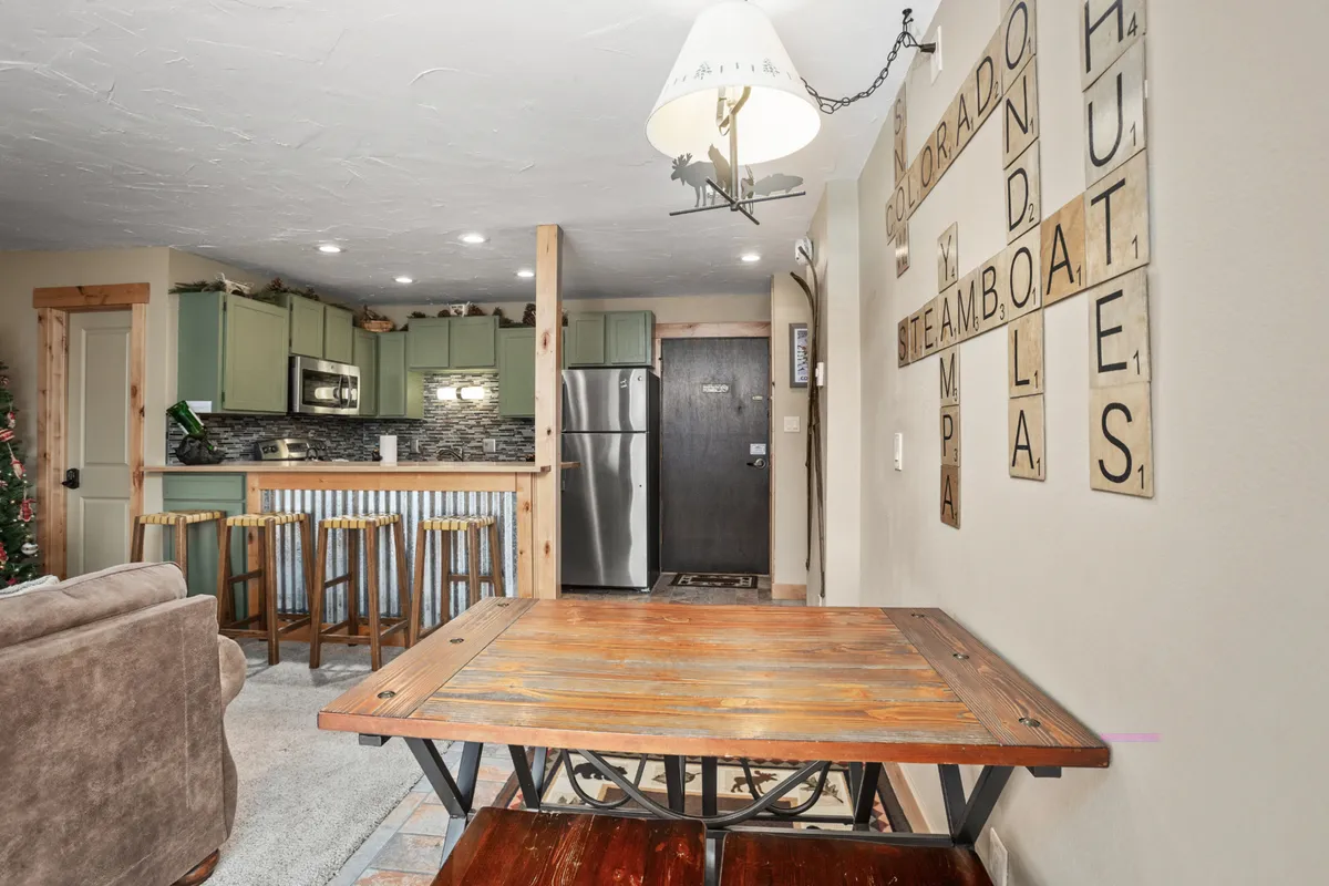 A welcoming dining area featuring a wooden table, bar stools at the kitchen counter, and tasteful wall art. The setting is ideal for sharing meals or gathering with friends and family, emphasizing communal and resort-style living.