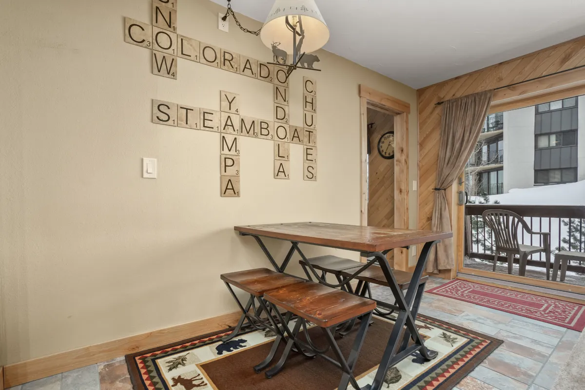 The image showcases a rustic wooden table surrounded by chairs, with scrabble-style wall art adding a playful touch. The setting is bright and inviting, suggesting a space for family meals or game nights after outdoor adventures.